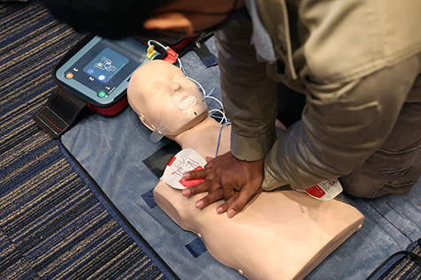 A man performing CPR with an AED on the ground